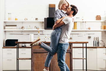 handsome boyfriend and attractive girlfriend hugging and standing in kitchen - obrazy, fototapety, plakaty