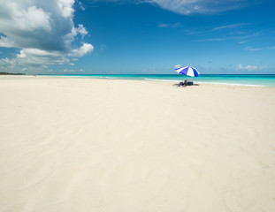 Fototapeta na wymiar Wonderful beach of Varadero during a sunny day, fine white sand and turquoise and green Caribbean sea,on the right one blue parasol,Cuba.concept photo,copy space.