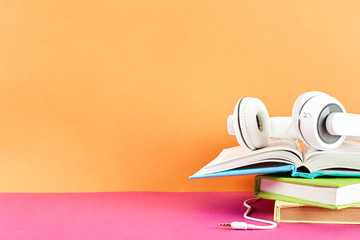 Electronic audiobook vs regular paper book concept. Stack of different color hardcover books with...