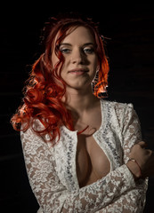 cheerful redhead girl in a transparent blouse with curly hair smiling on a dark background.