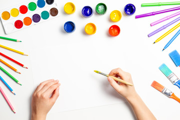 Kid hands painting at the table with art supplies, top view