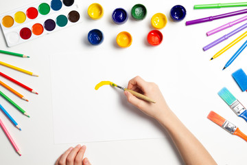 Kid hands painting at the table with art supplies, top view
