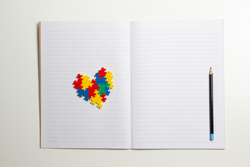 Open notebook, pencil and heart made of plastic construction bricks on white background