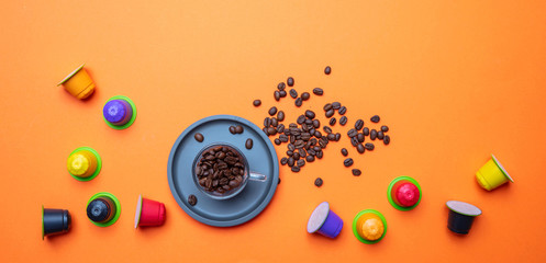 Coffee cup, beans and capsules on orange color background, copy space, top view