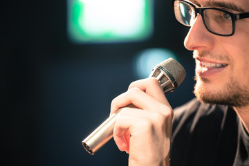 Speaker on the stage: Young Caucasian man is talking into a mirophone