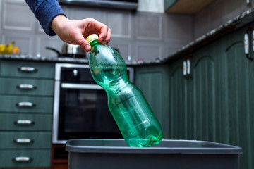 Close up of a person throwing empty plastic bottle into the trash bin  in the kitchen. Plastic recycling and waste separation