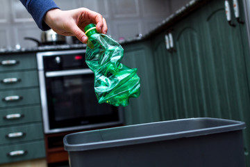 Close up of a person throwing empty plastic bottle into the trash bin  in the kitchen. Plastic recycling and waste separation