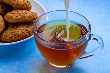 Breakfast with oatmeal cookies and pouring milk into a cup of black tea. Flour, cereal dessert and hot drink