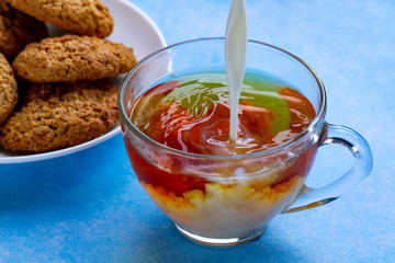 Breakfast with oatmeal cookies and pouring milk into a cup of black tea. Flour, cereal dessert and hot drink