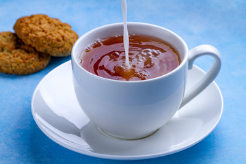 Breakfast with oatmeal cookies and pouring milk into a cup of black tea. Flour, cereal dessert and hot drink