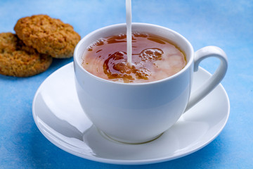 Breakfast with oatmeal cookies and pouring milk into a cup of black tea. Flour, cereal dessert and hot drink