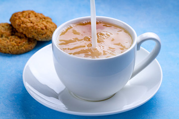 Breakfast with oatmeal cookies and pouring milk into a cup of black tea. Flour, cereal dessert and hot drink