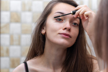 Young, attractive brown hair woman applying black mascara for eyelash makeup in mirror. Home and everyday Makeup