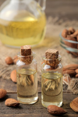 natural almond oil in a glass bottle and fresh almond nuts close-up on a brown wooden table.