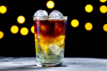 Refreshing cocktail with ice cubes and soda bubbles on the background of lights. Ice coffee. Cold and carbonated drinks