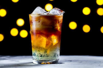 Refreshing cocktail with ice cubes and soda bubbles on the background of lights. Ice coffee. Cold and carbonated drinks
