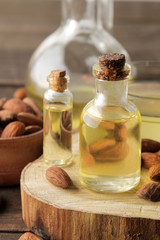 Fototapeta na wymiar natural almond oil in a glass bottle and fresh almond nuts close-up on a brown wooden table.