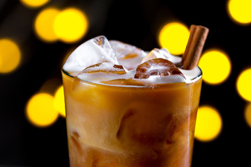 Сoffee, refreshing cocktail with ice cubes, foam and cinnamon on the background of lights. Cold drinks