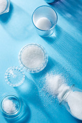Closeup of scattered sugar and sugar in a glass bottle, on blue background
