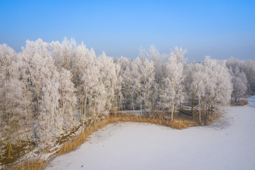 Rime and hoarfrost covering trees. Aerial view of the snow-covered forest and lake from above. Winter scenery. Landscape photo captured with drone.