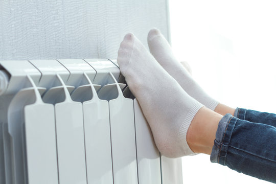 Young woman warming her legs on the battery at home