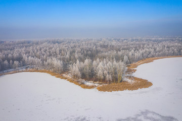 Fototapeta na wymiar Rime and hoarfrost covering trees. Aerial view of the snow-covered forest and lake from above. Winter scenery. Landscape photo captured with drone.