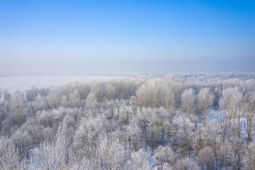 Rime and hoarfrost covering trees. Aerial view of the snow-covered forest and lake from above. Winter scenery. Landscape photo captured with drone.