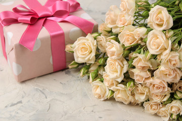 A bouquet of beautiful tender mini roses and a gift box on a light concrete background. holidays. presents