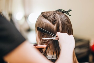 hairdresser makes hairstyle for young woman in beauty salon