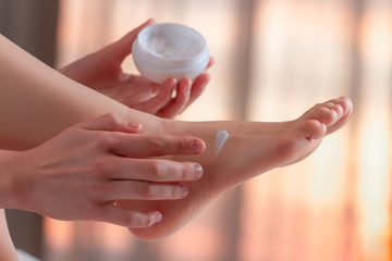 Young woman caring about her feet and applying hydrating, moisturizing cream. Foot and skin care.