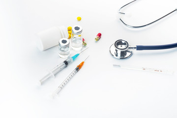 Pills spilling out of pill bottle syringe thermometer and stethoscope on white background