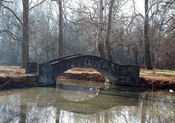 Fototapeta na wymiar The old stone footbridge in the park on a winter day.