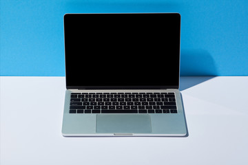 laptop with blank screen on white desk and blue background