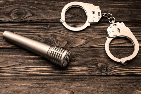handcuffs, microphone on wooden background. violation of copyright law.