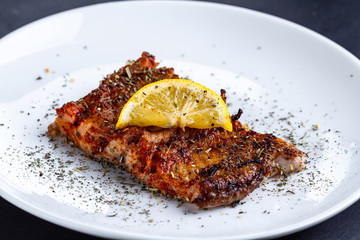 Fresh, grilled salmon fillet with a slice of juicy lemon, spices and herbs on a white plate