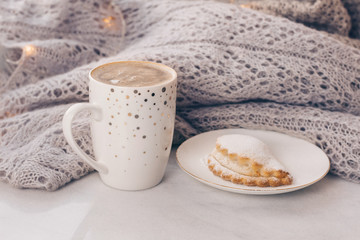Stack of warm cozy knitwears and a cup of coffee on white marble windowsill against white window background. Copy space.
