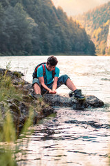 Young boy taking pure water from a river and holding it in the hands