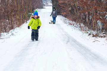 Fototapeta na wymiar Little son with mother sliding in the snow in winter park. Happy young family enjoying a sledge ride. Winter holidays. Young happy family enjoying winter snowy weather. Christmas vacation.
