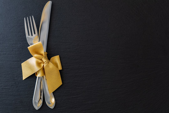 fork and knife with golden ribbon on slate tray