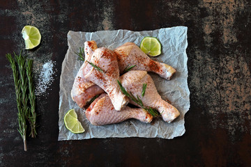 Raw chicken legs with rosemary and spices on paper.