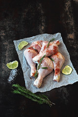 Raw chicken legs with rosemary and spices on paper.