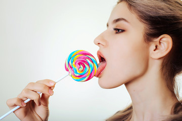 An attractive girl licks a multi-colored Lollipop.