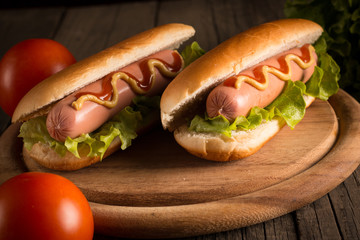 Photo of barbecue grilled hot dog with yellow mustard and ketchup on wooden background. Hot dog sandwich with potato fries and sauces.