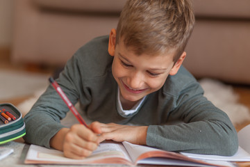 Smiling boy doing homework on the floor