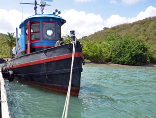 Up the dockline to the bow of a brightly painted red, blue, and black tug boat with old tires...