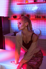 beautiful elegant woman sitting on kitchen counter and posing in neon pink light