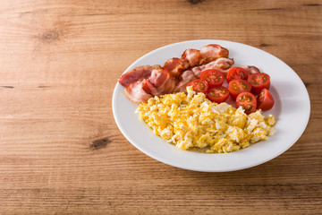 Breakfast with scrambled eggs, bacon and tomatoes on wooden table. Copyspace