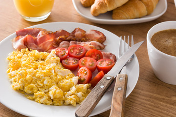Breakfast with scrambled eggs, bacon, tomatoes,coffee,orange juice ,croissant and corn flakes on wooden table