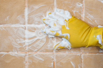 Hand in yellow gloves with sponge washing the tile. Cleaning concept.