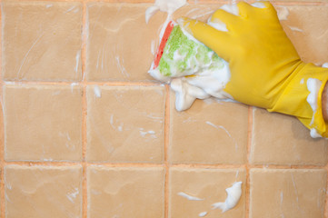 Hand in yellow gloves with sponge washing the tile. Cleaning concept.